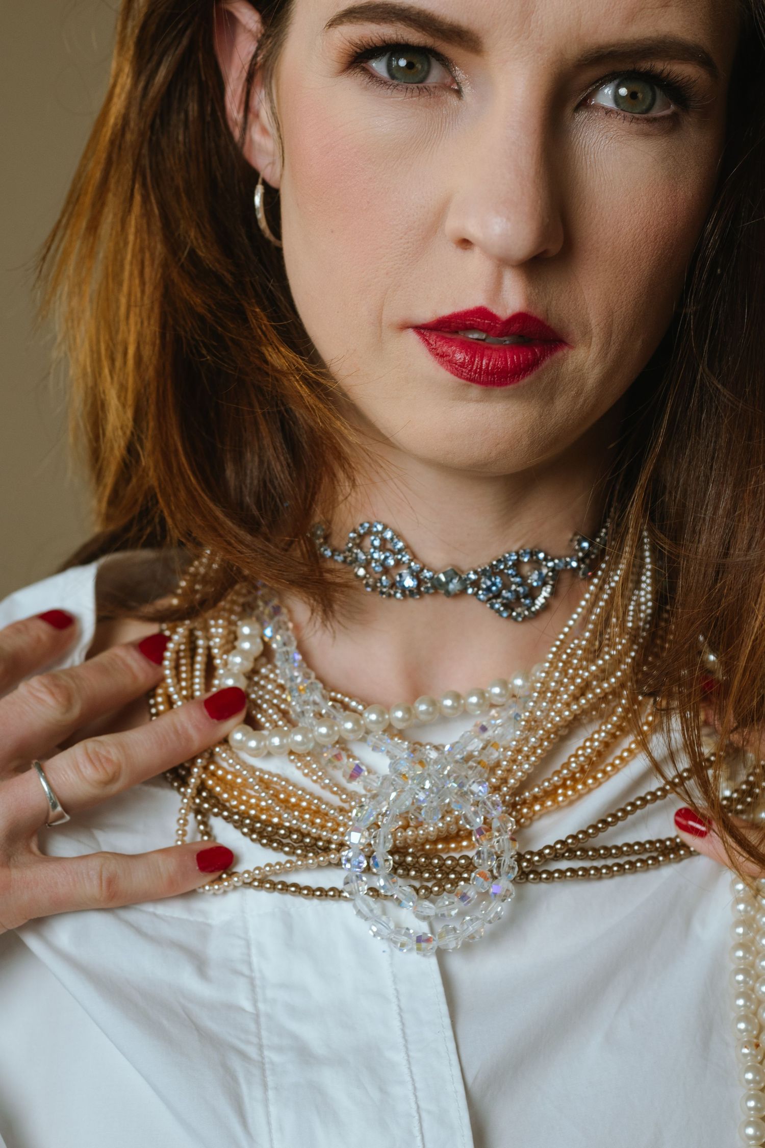 Layered pearl and gold statement necklaces styled with a crisp white collared shirt and red lipstick.