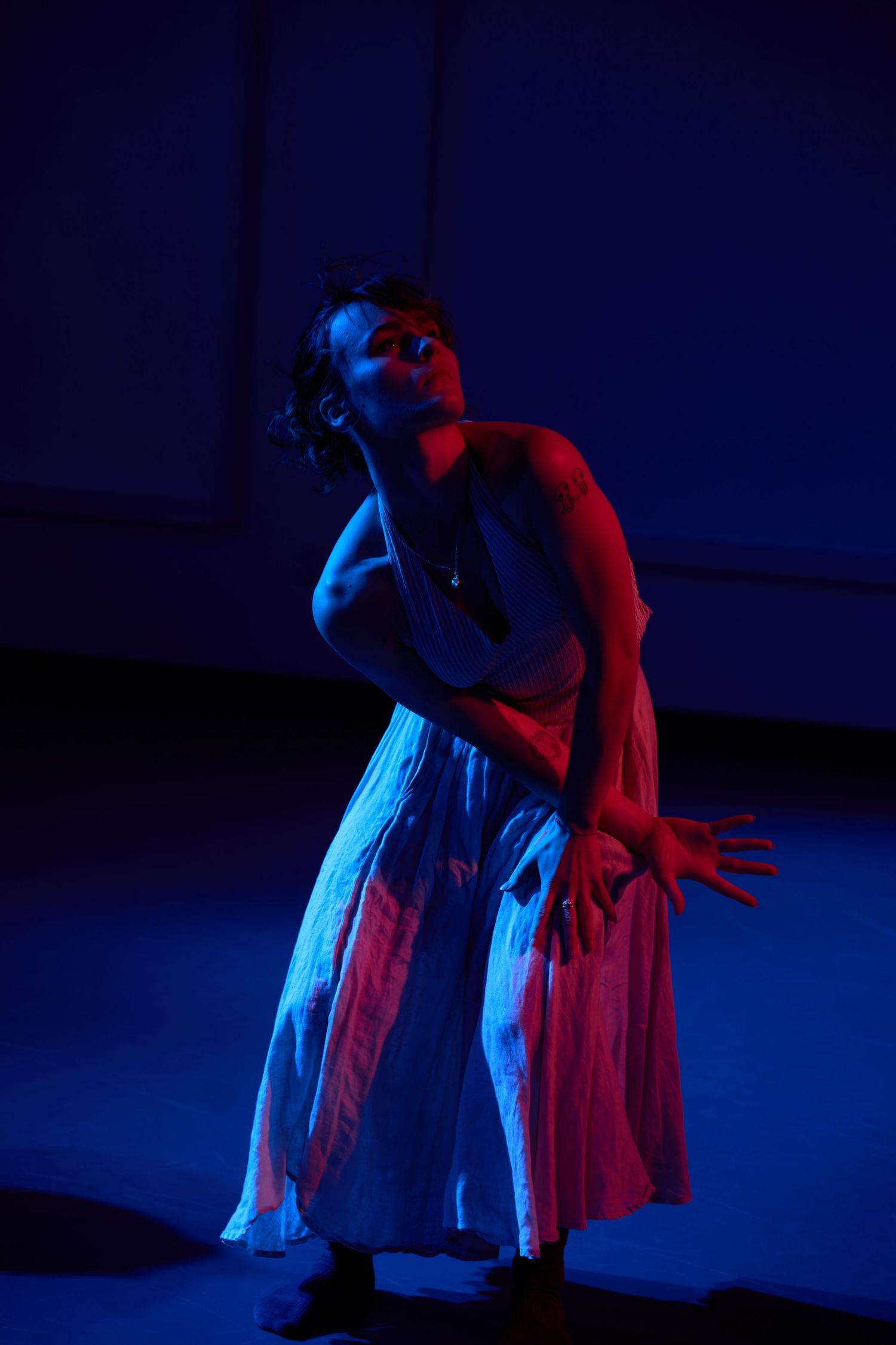 Dancer in white dress poses dramatically under blue and red stage lighting in a theatrical performance.