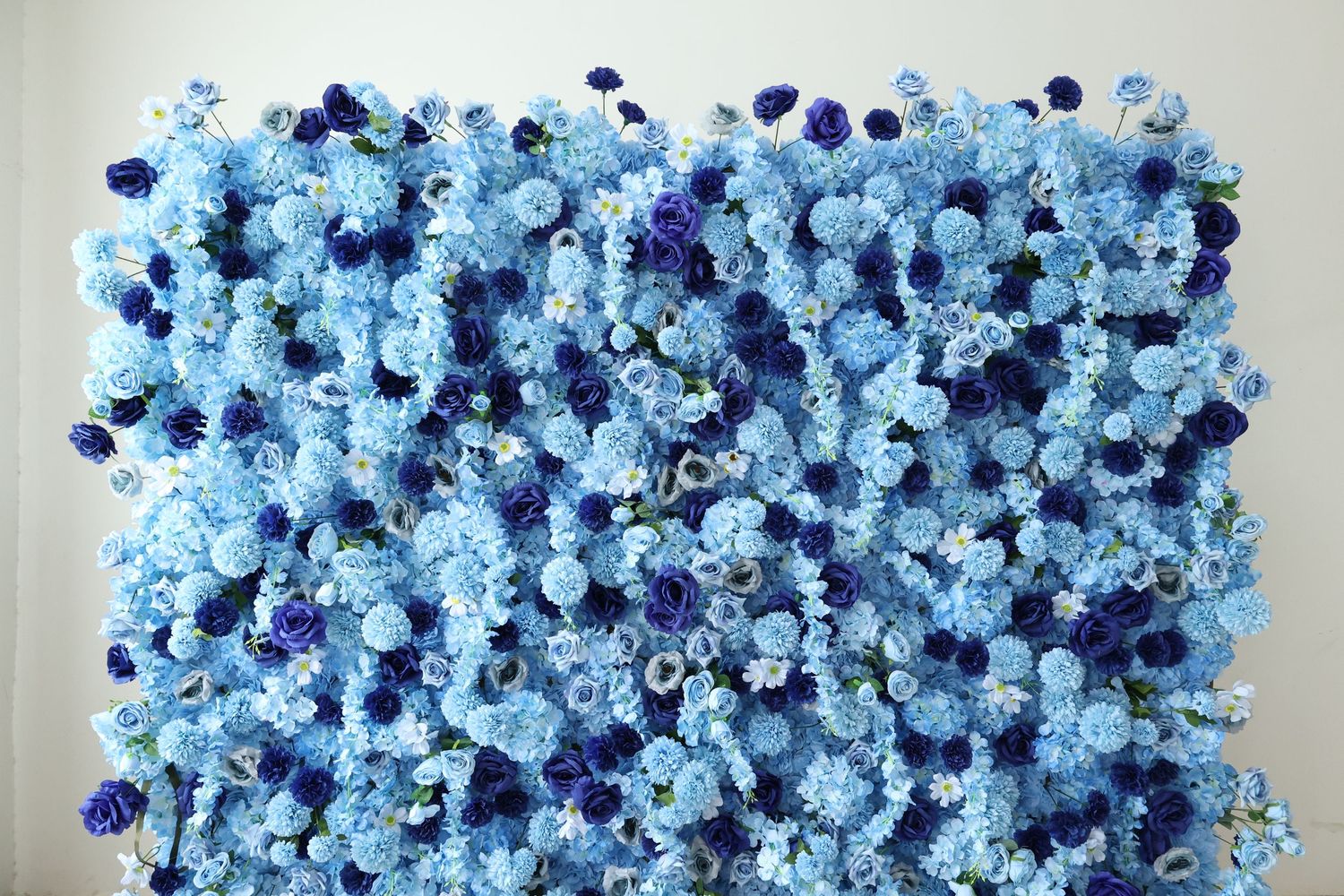 A lush flower wall backdrop featuring blue and dark blue roses and hydrangeas for weddings or events.