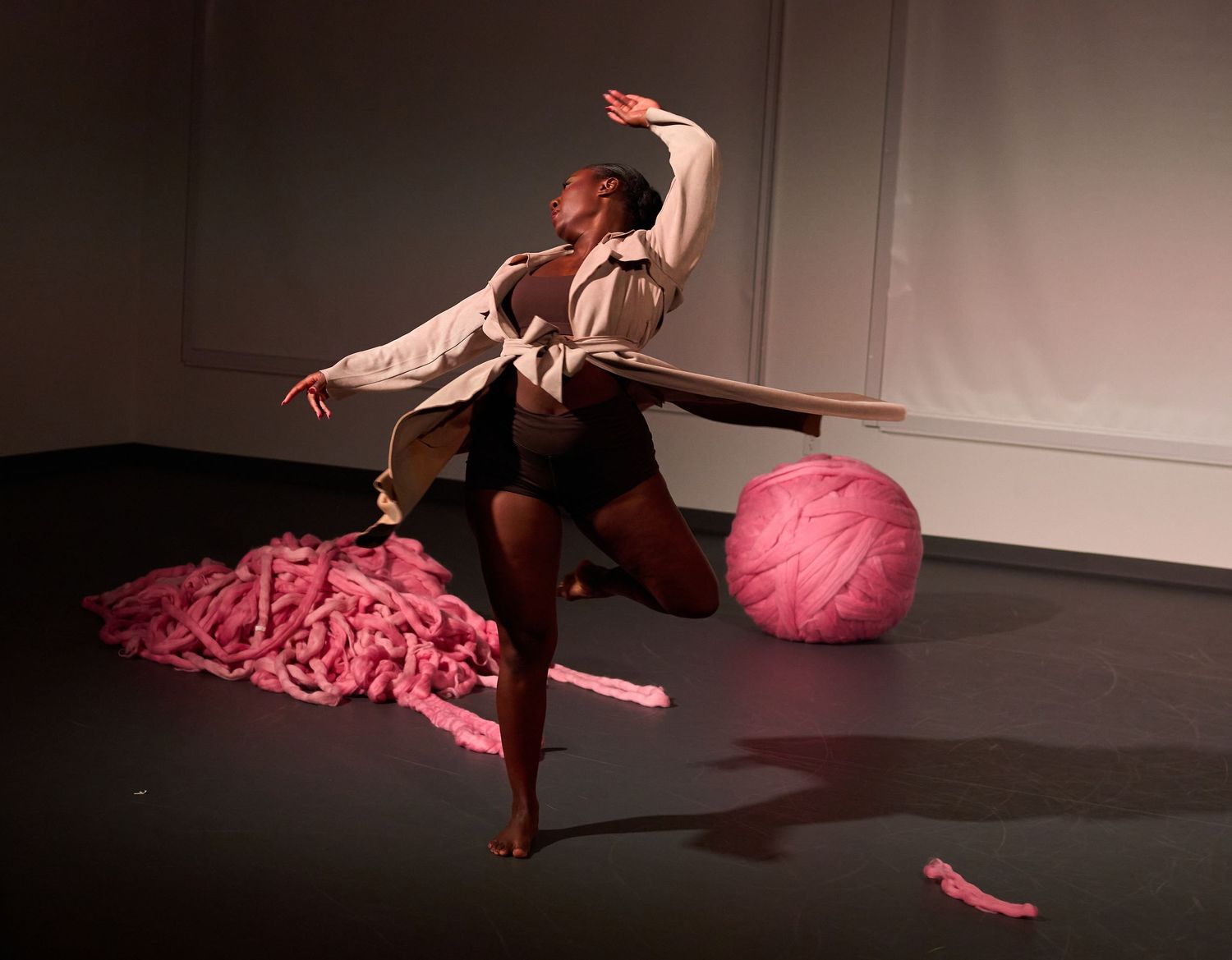 Dancer poses dramatically on stage beside a large pink yarn ball and pile of pink ribbons during a performance.