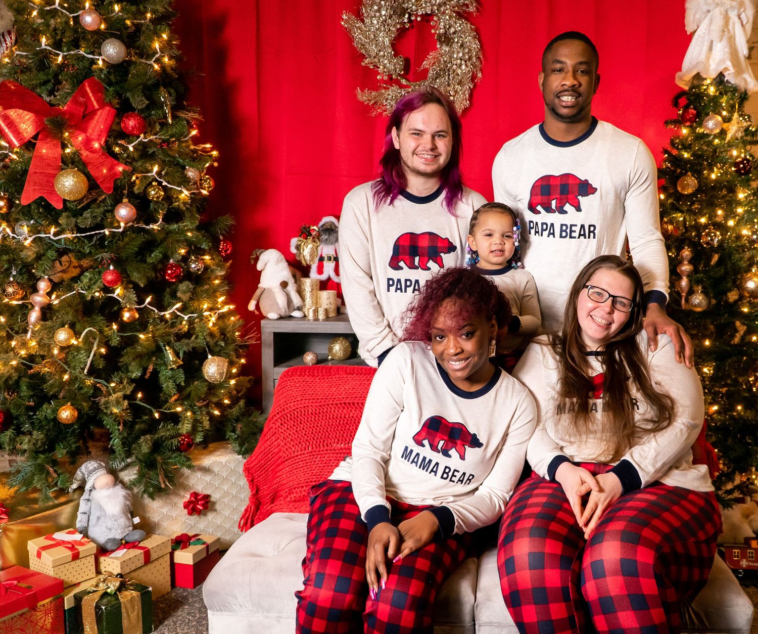 Family in matching Papa Bear and Mama Bear Christmas pajamas posing by a decorated tree.