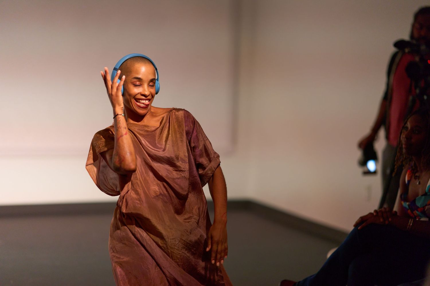A smiling woman in a flowing brown dress and blue headband walks gracefully on a fashion runway.