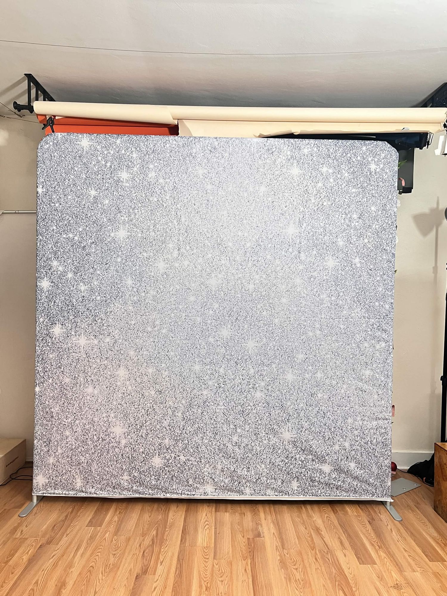 Sparkling silver glitter photo booth backdrop on a metal stand in a photography studio.