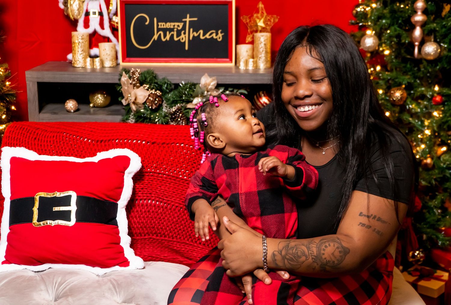 Smiling mother holding baby in red plaid outfit during festive Christmas photo session.