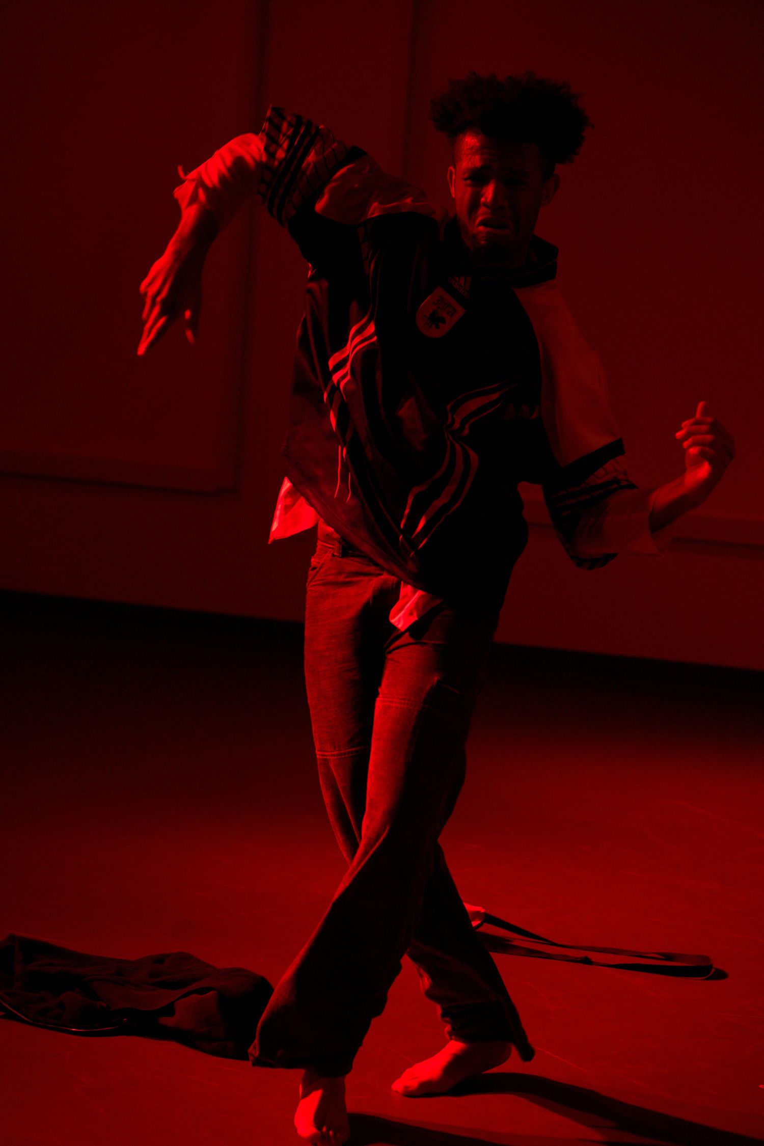 A dancer performs expressive modern dance moves under dramatic red stage lighting in a dark studio.