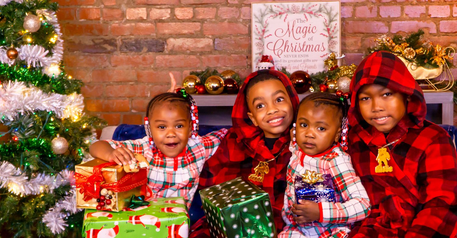 Four children in red plaid pajamas posing with Christmas gifts by decorated tree.