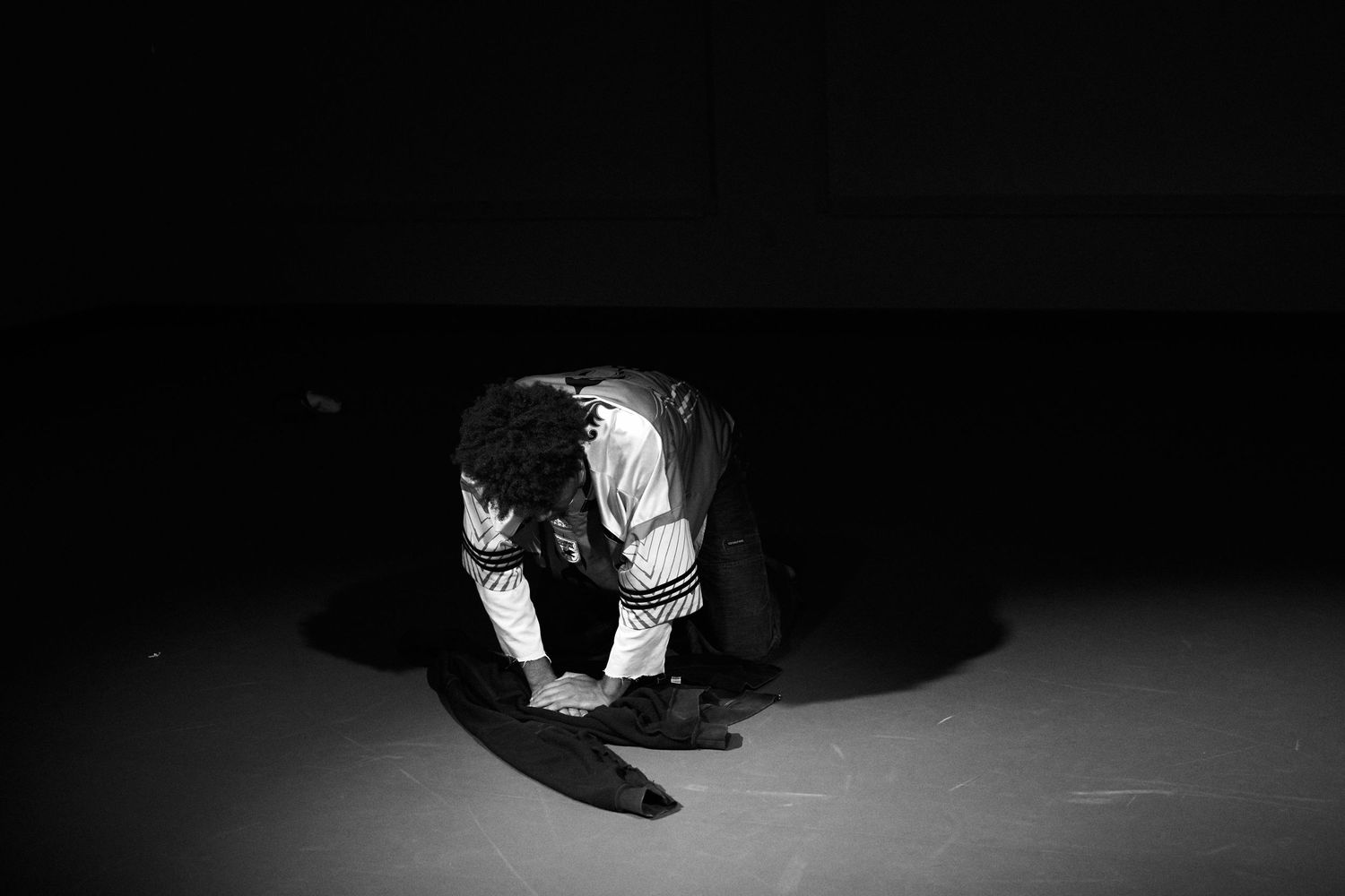Black and white photo of a person bowing down on a dark stage floor in traditional costume.