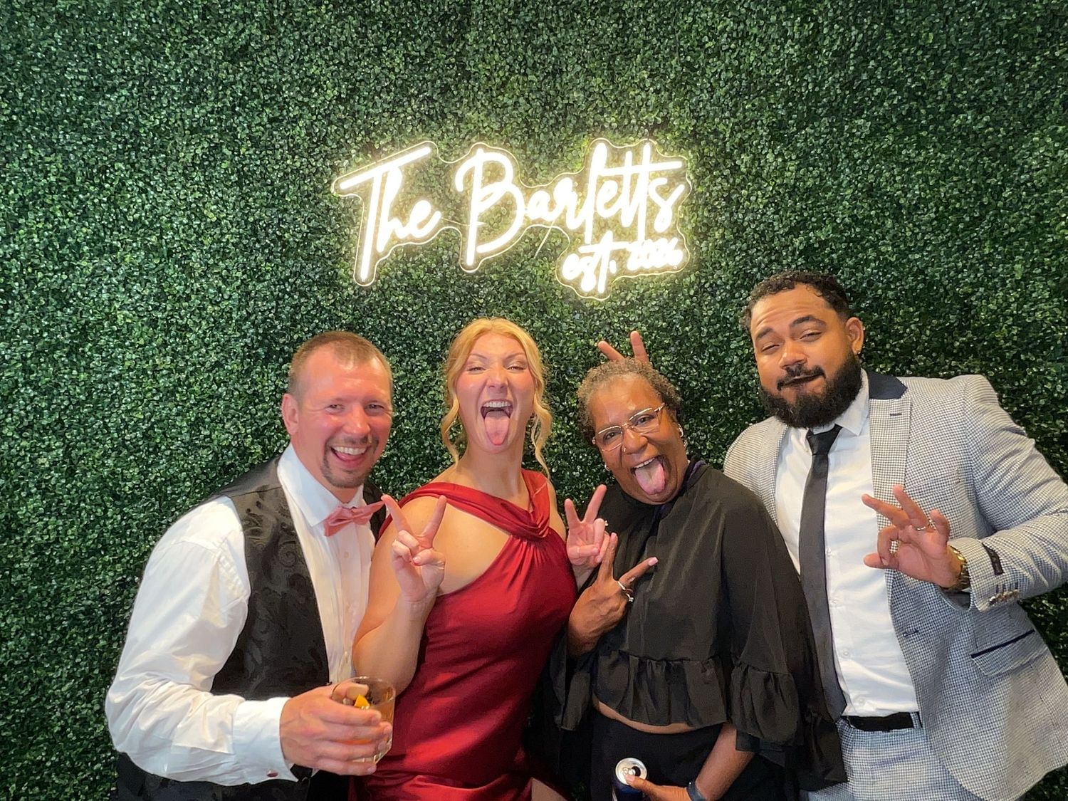 Four friends smile and pose in front of The Bartletts neon sign at a wedding reception photo booth in Heinz History Center.