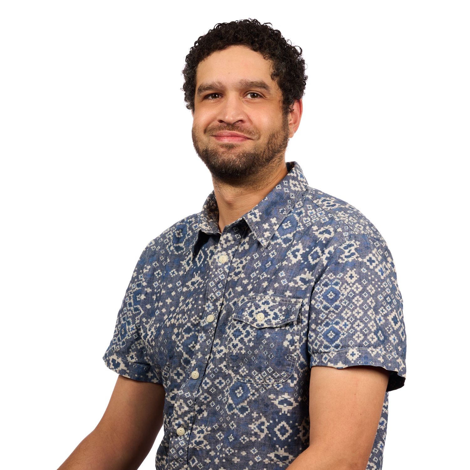 Smiling man in a blue patterned short-sleeve shirt posing against a white background.