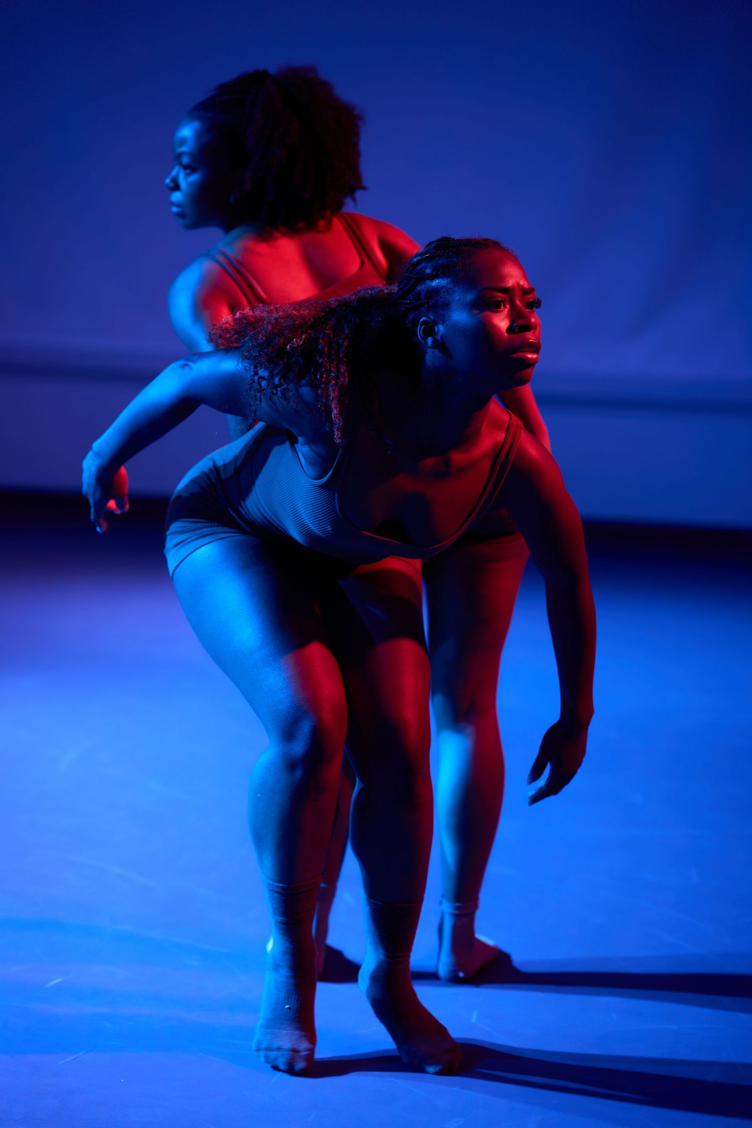 Two female dancers perform contemporary dance under dramatic red and blue stage lighting.