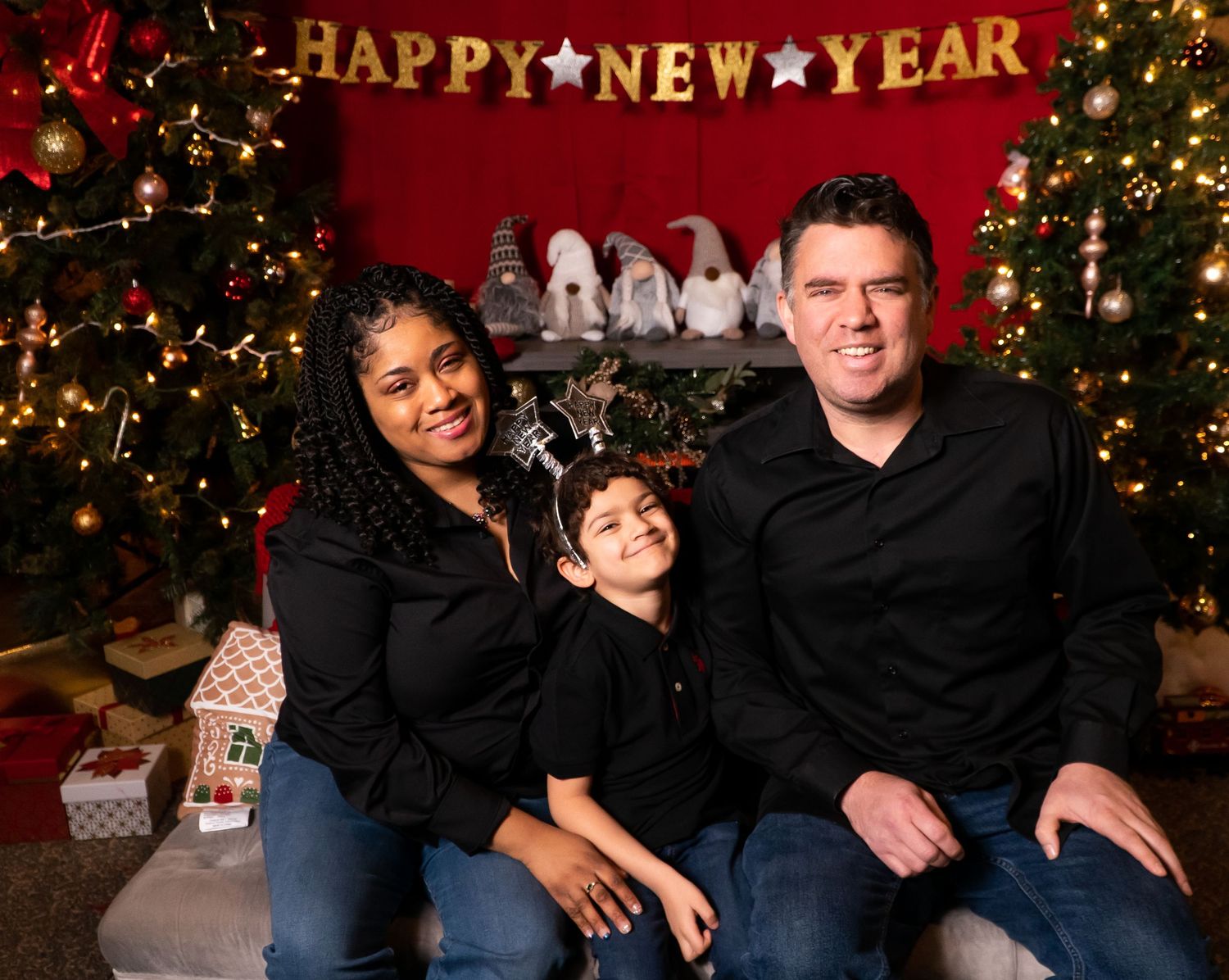 Family of three posing in front of Happy New Year banner with Christmas trees.