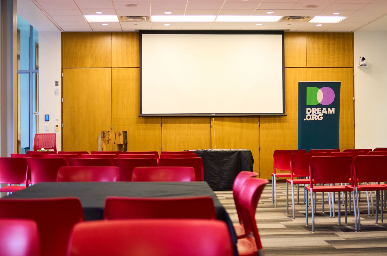 Conference room with red chairs, projection screen, and a Dream Jobs banner on wooden panel wall.
