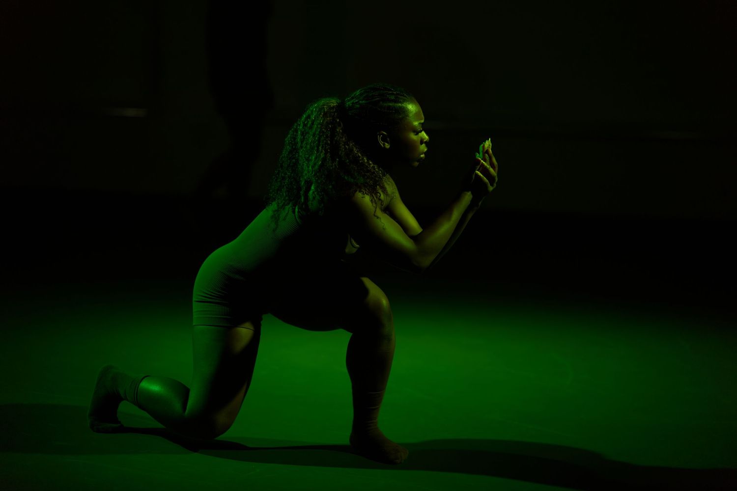 Athlete in a lunge position under dramatic green lighting in a dark studio setting.