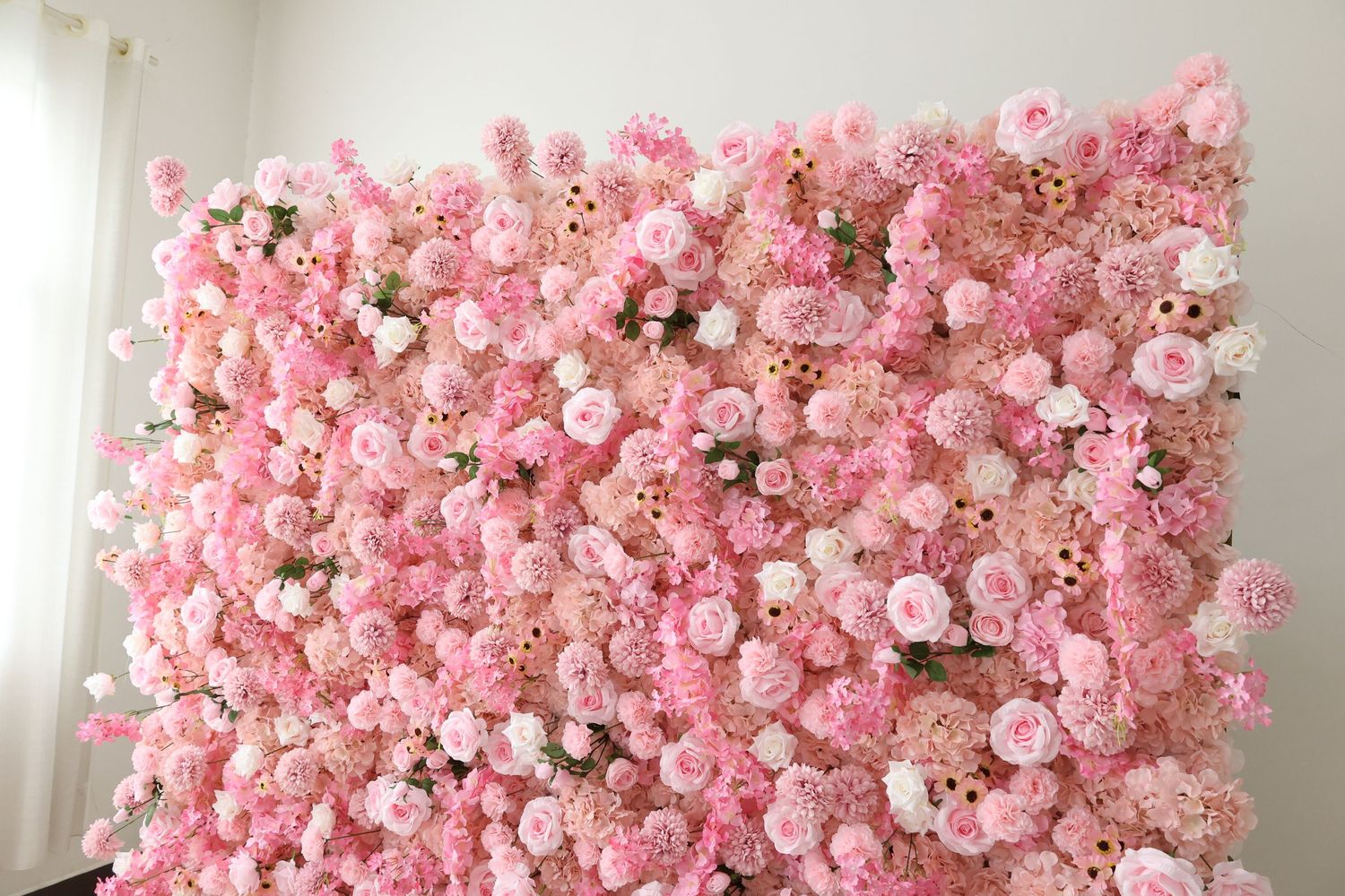 A lush pink flower wall backdrop featuring roses and peonies in soft pink and white hues, perfect for events.