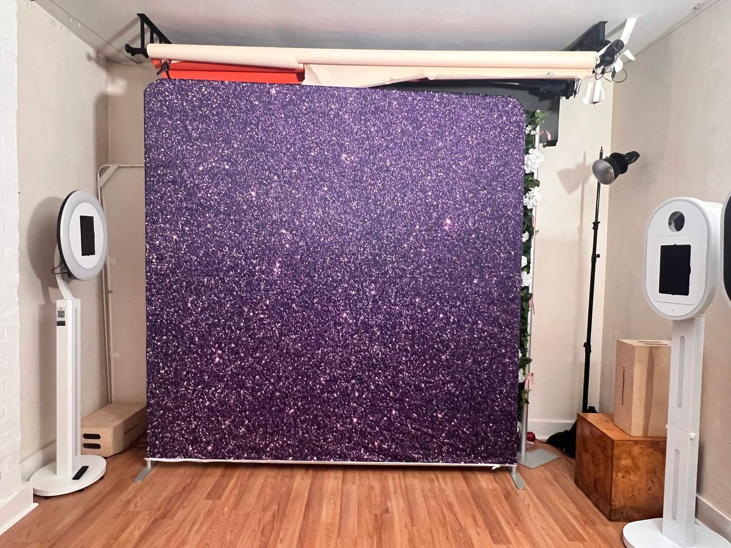 Purple glitter sparkle photo booth backdrop on a metal stand in a photography studio.