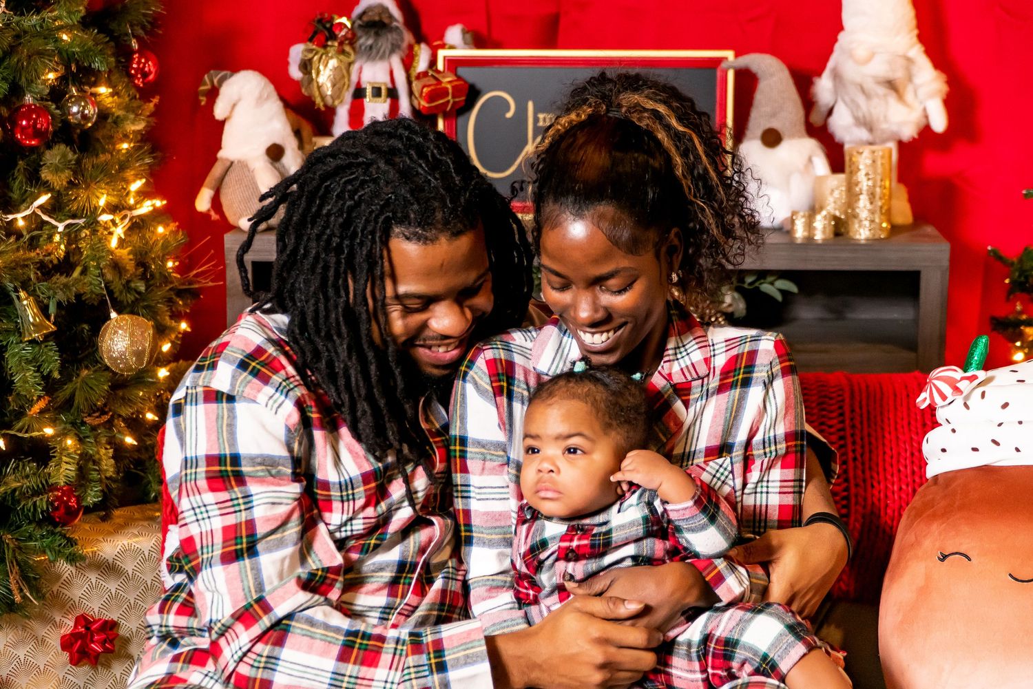 Family of three in matching plaid Christmas pajamas share a joyful holiday portrait.