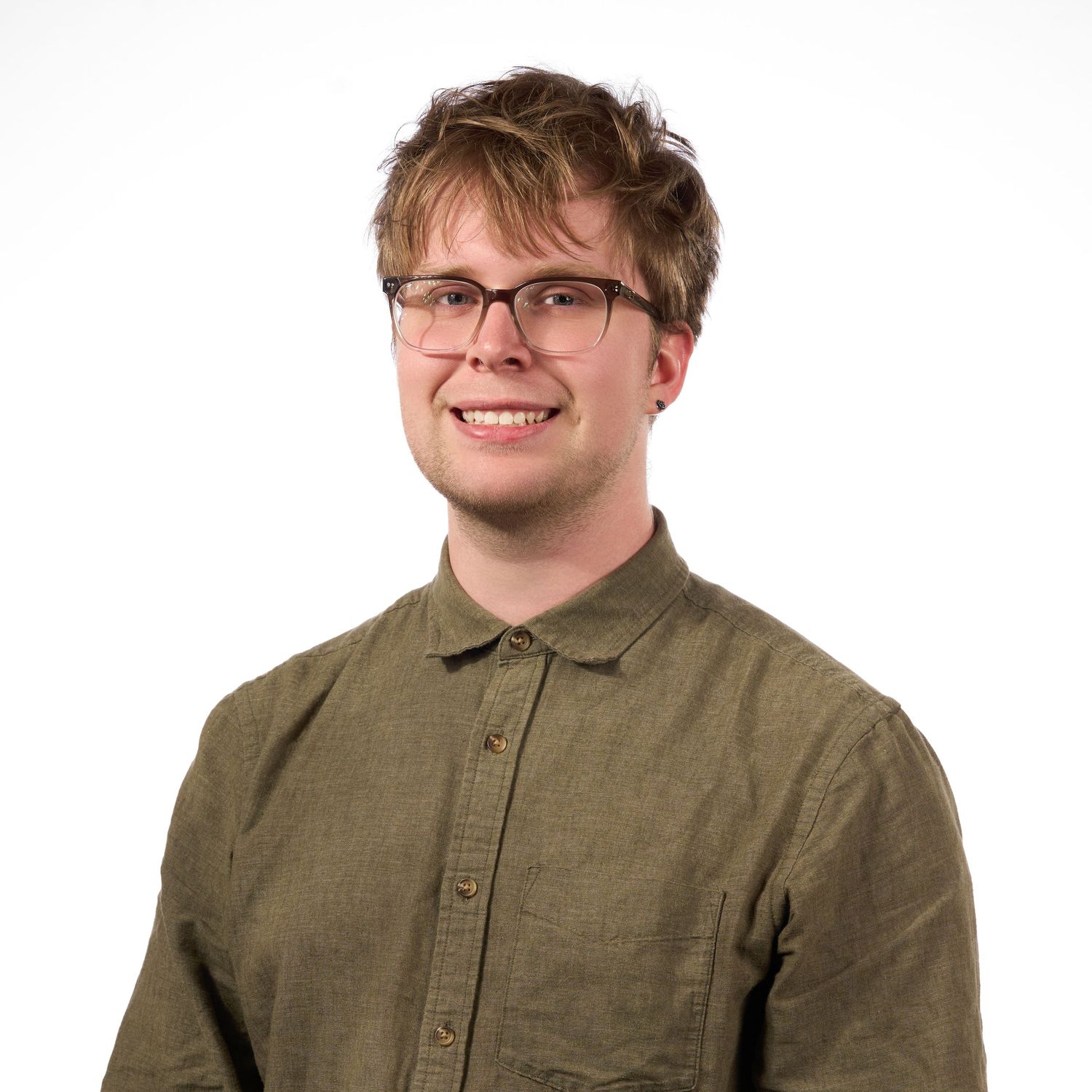 Young man with glasses and short brown hair smiling, wearing an olive green linen shirt against a white background.