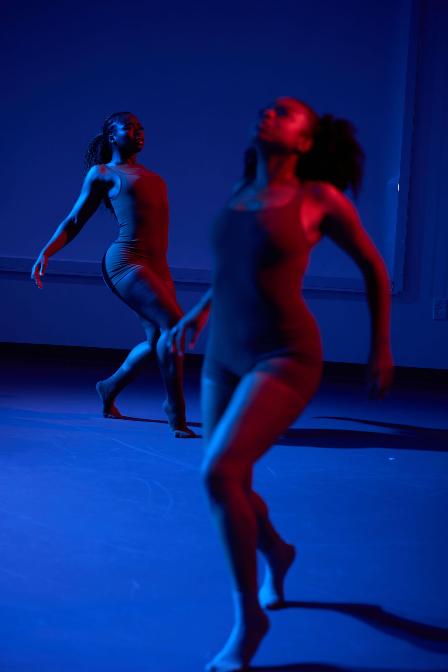Two dancers perform contemporary dance under dramatic blue and red stage lighting in a studio.