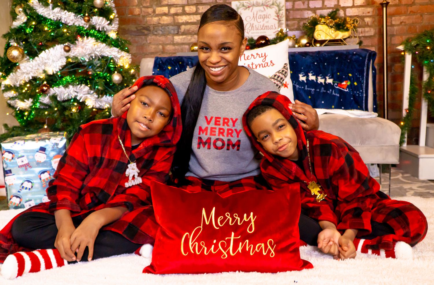 Mother wearing Very Merry Mom shirt with two sons in red plaid pajamas at Christmas.