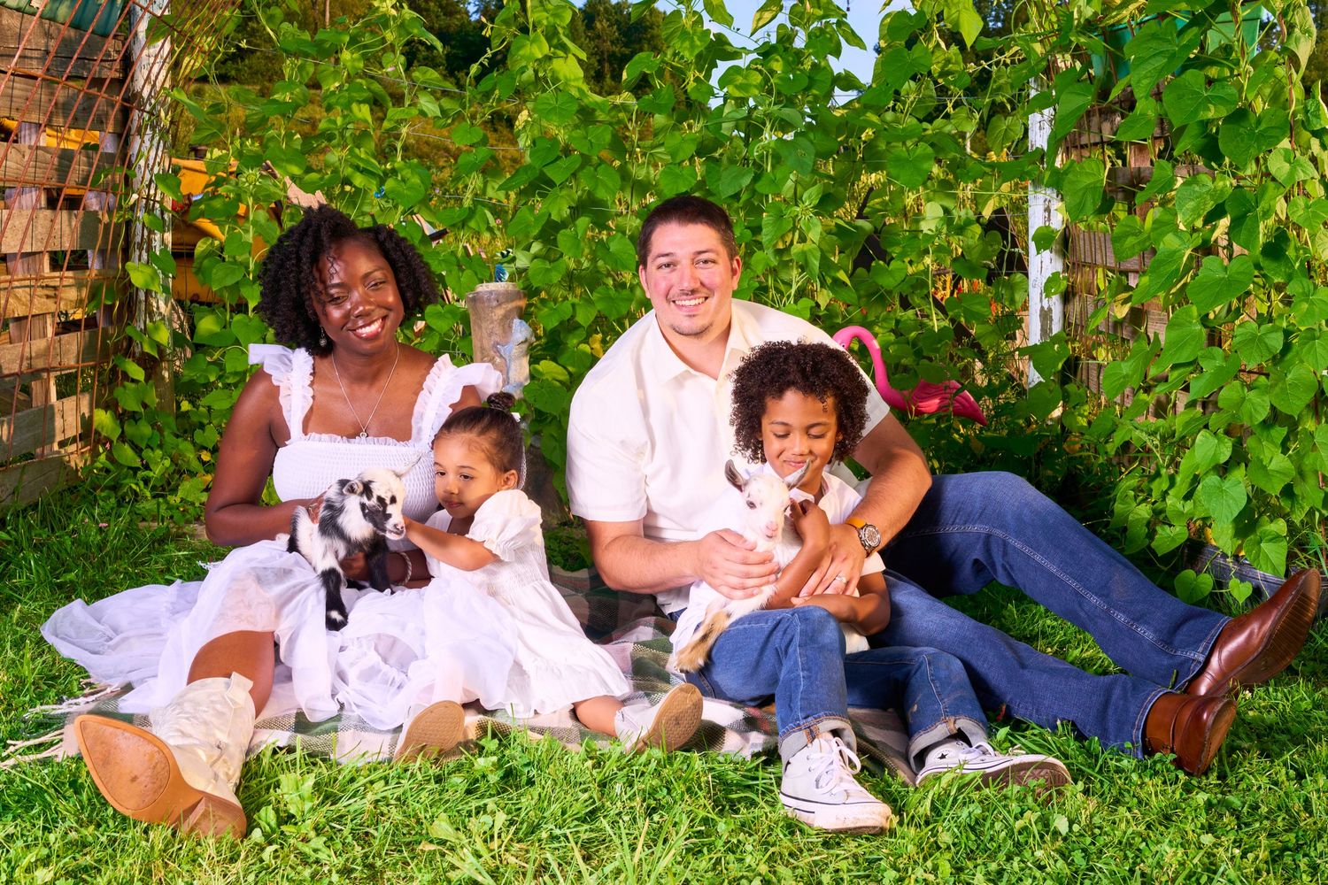 Happy interracial family with two children and puppies sitting on green grass outdoors in a garden setting.