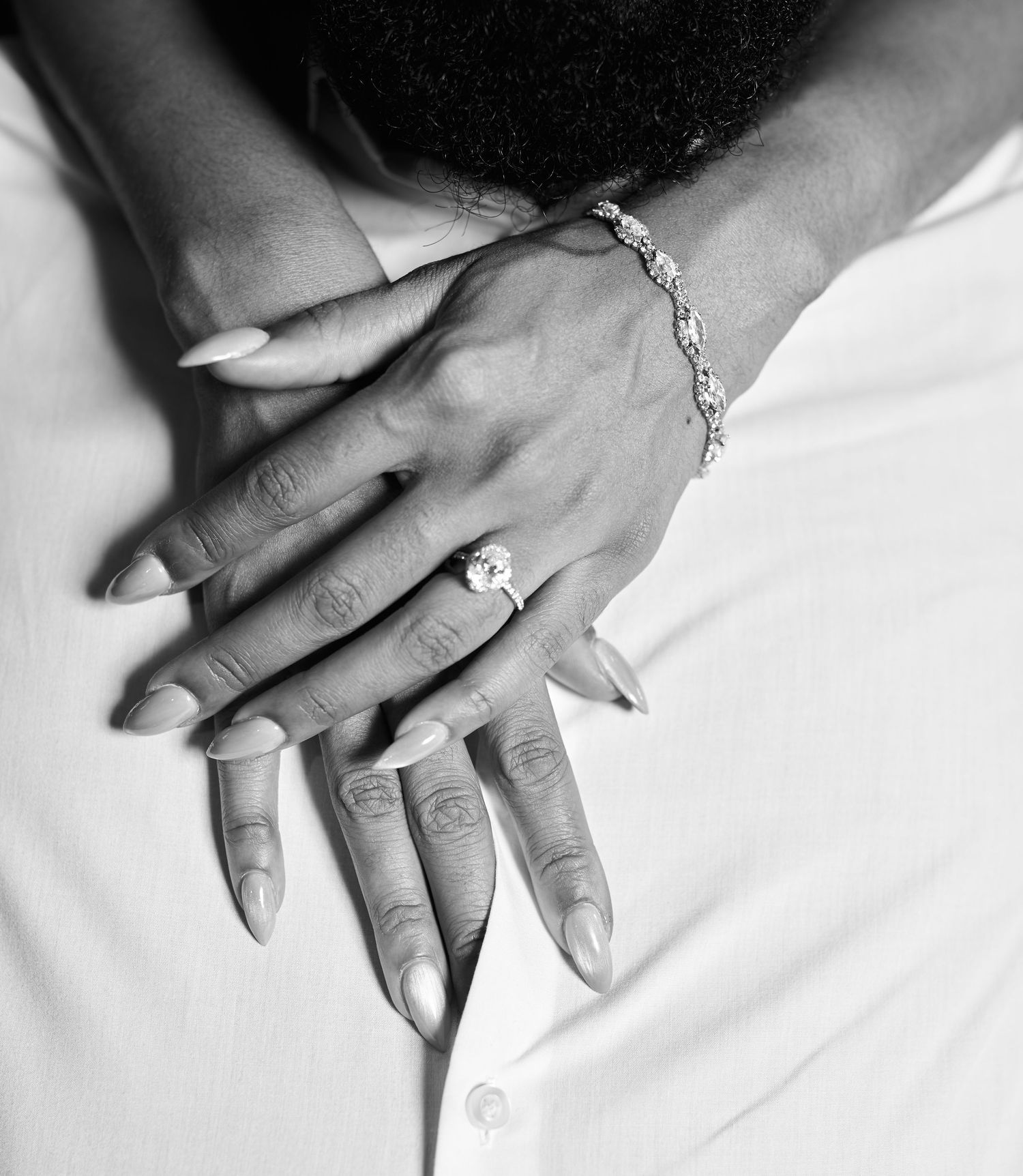 Close-up black and white photo of a womans hand wearing a diamond engagement ring and tennis bracelet.