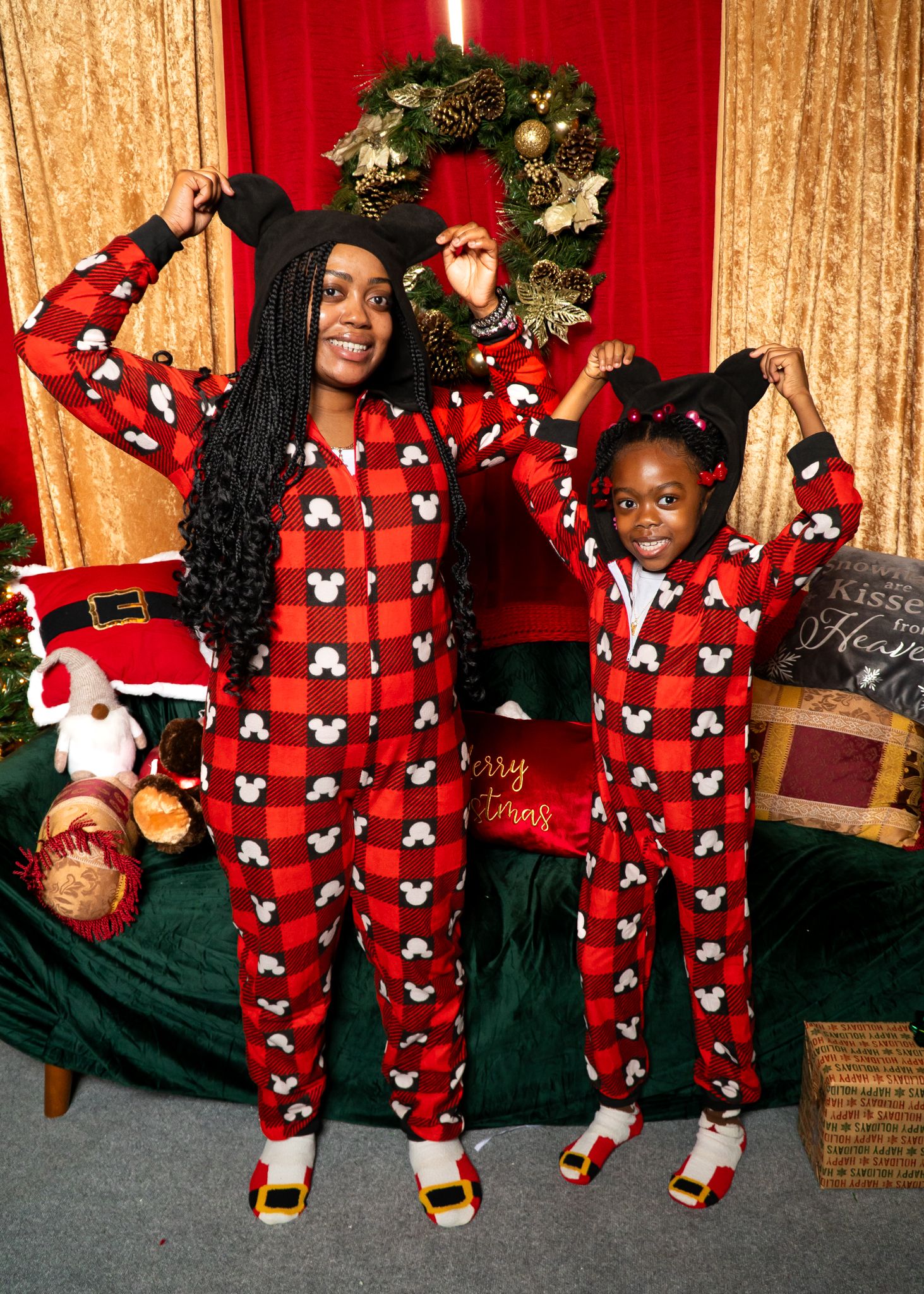 Mom and child in matching red Mickey Mouse plaid onesies posing playfully in a festive Christmas decorated room.
