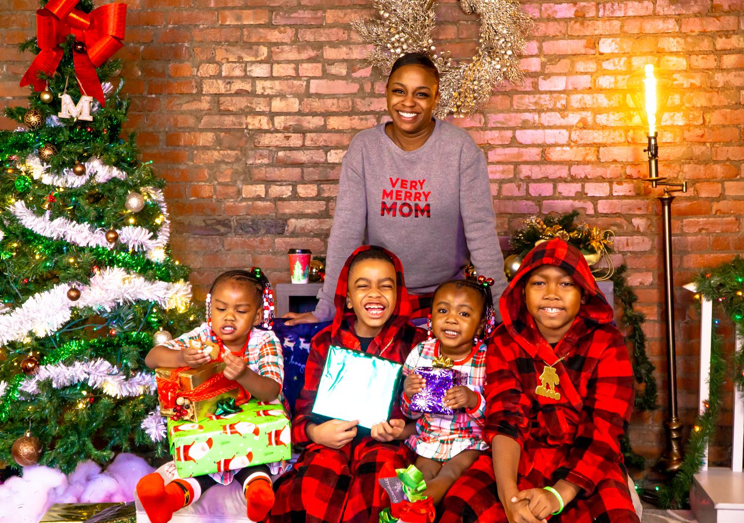Mother in Very Merry Mom shirt with four children in plaid pajamas at Christmas tree.