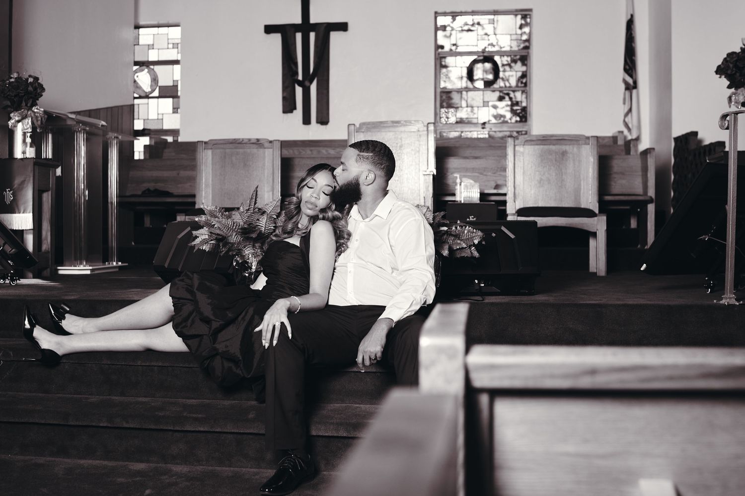Black and white photo of a couple sharing a romantic moment sitting in a church pew.