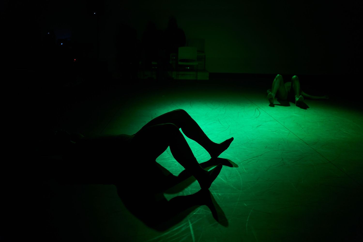 Silhouette of a person lying on a floor bathed in dramatic green light in a dark room.
