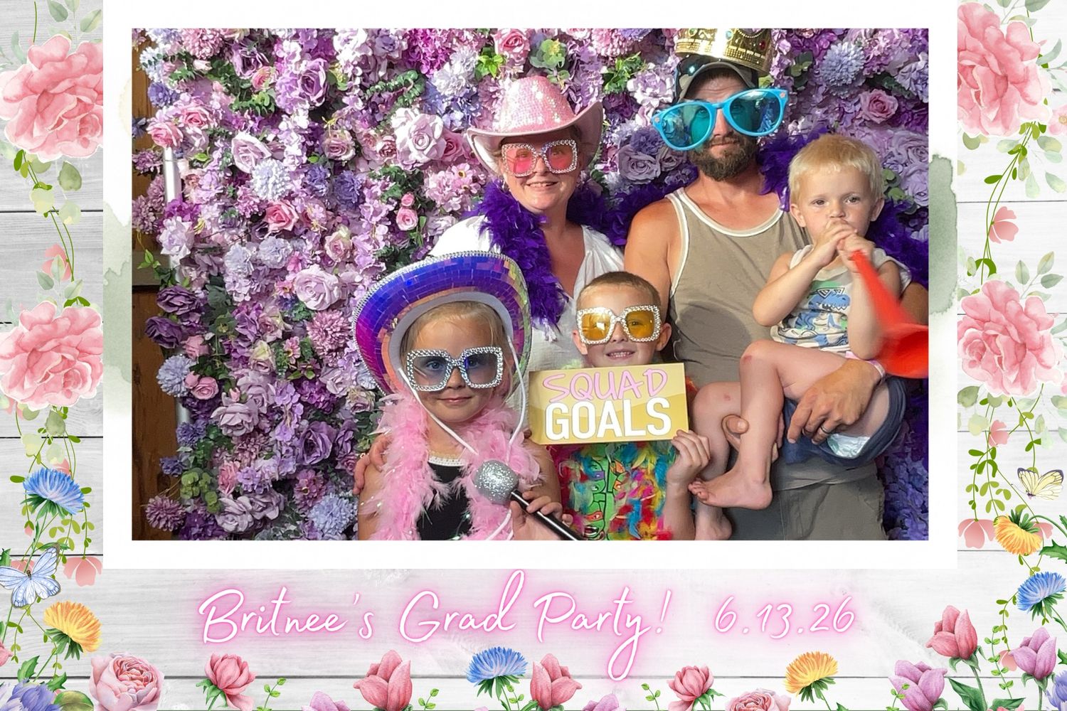 Family and friends celebrate Betnee's Grad Party on 6.19.24, posing with fun props in front of a floral backdrop.