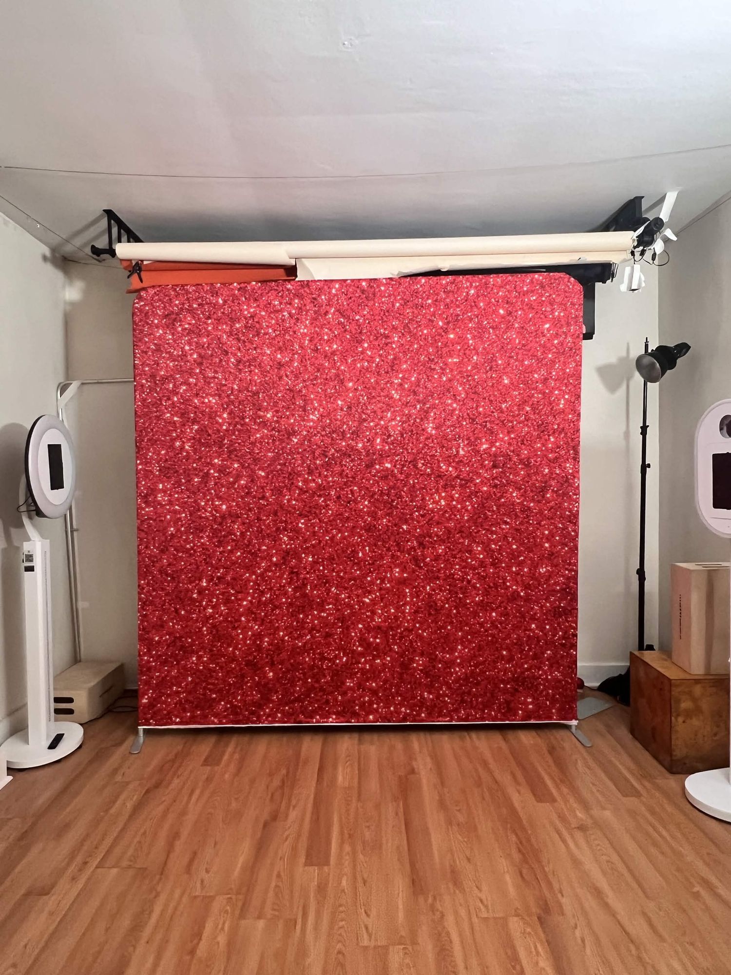Red glitter sparkle photo booth backdrop on a metal stand in a photography studio.