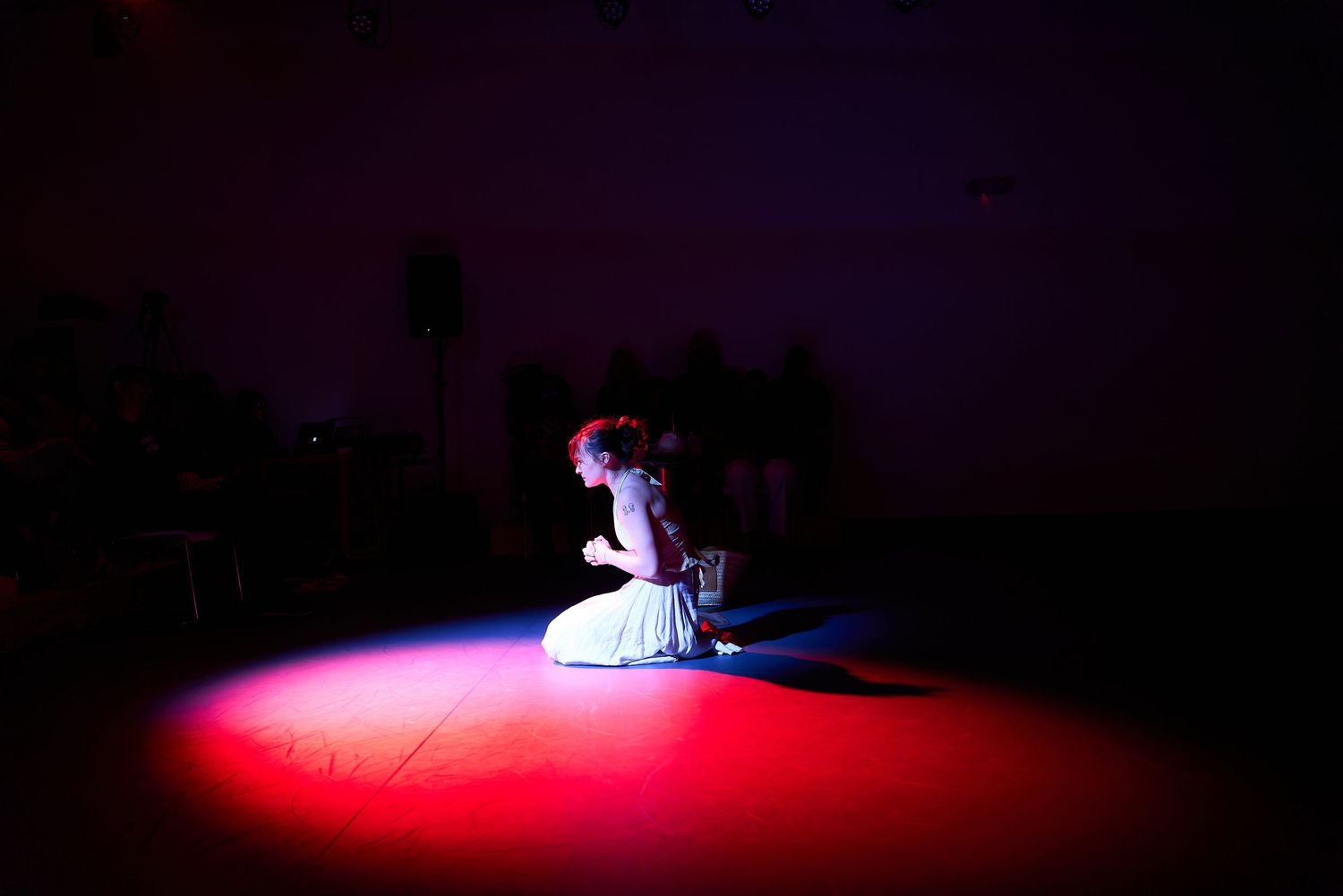 A dancer in white dress performs solo under dramatic red spotlight on dark stage.