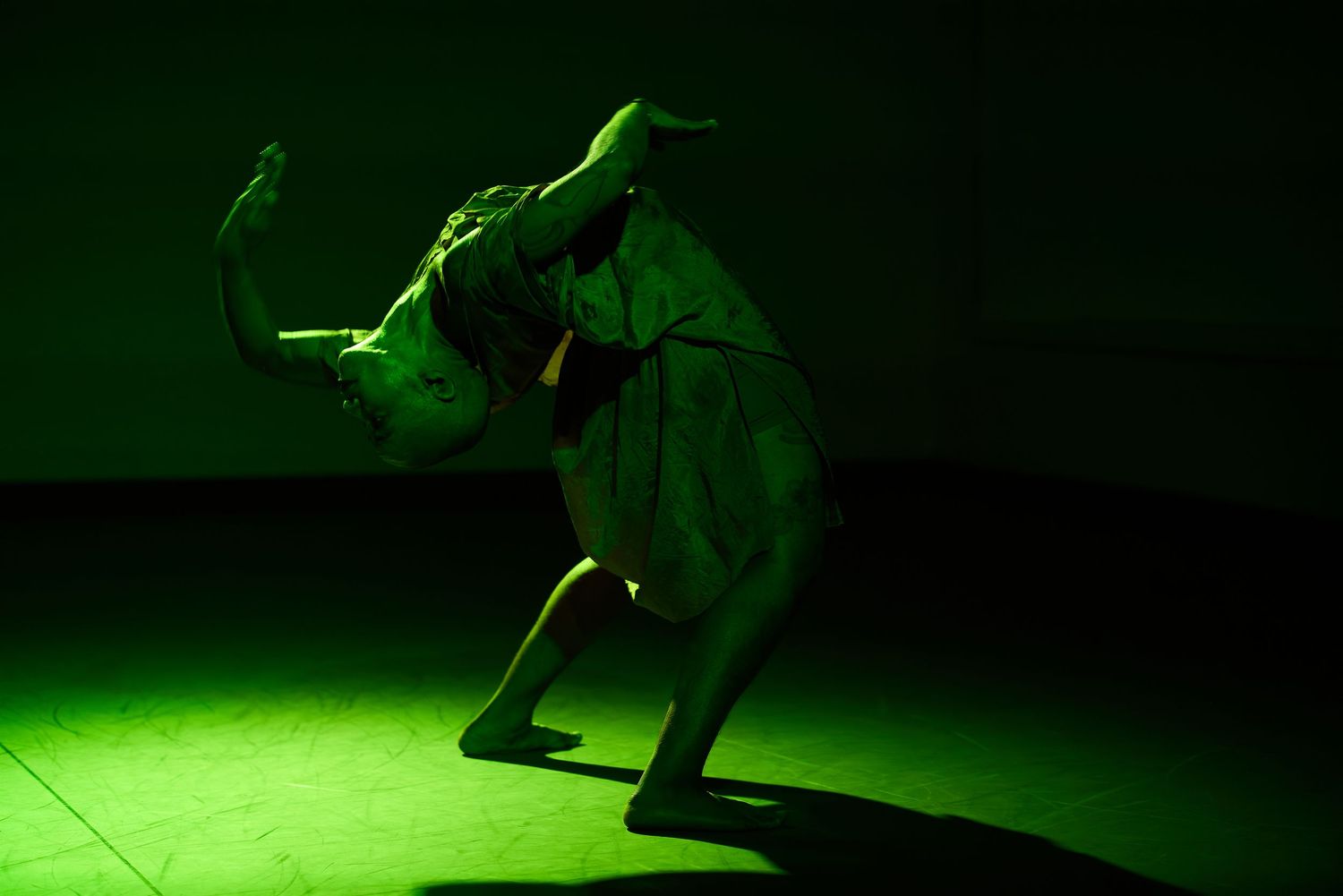 Dancer performing dramatic pose under green stage lighting in theatrical costume.