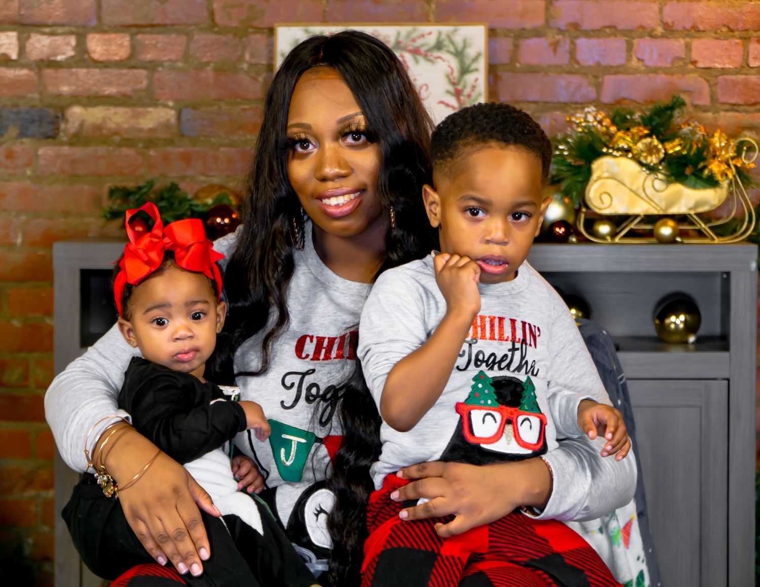 Mother holding infant daughter and young son in matching Christmas pajama outfits.