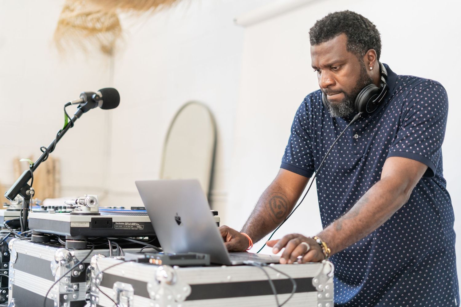 DJ performs at an event using turntables and laptop equipment while wearing a polka dot shirt.