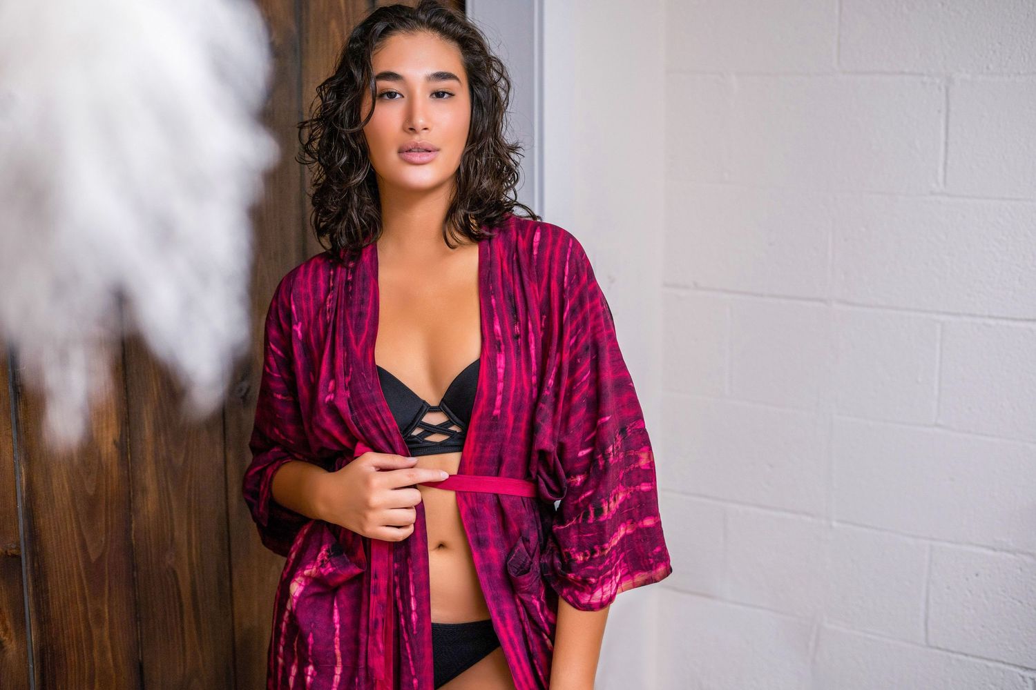 Fashion model wearing burgundy velvet robe and black lingerie in studio setting.