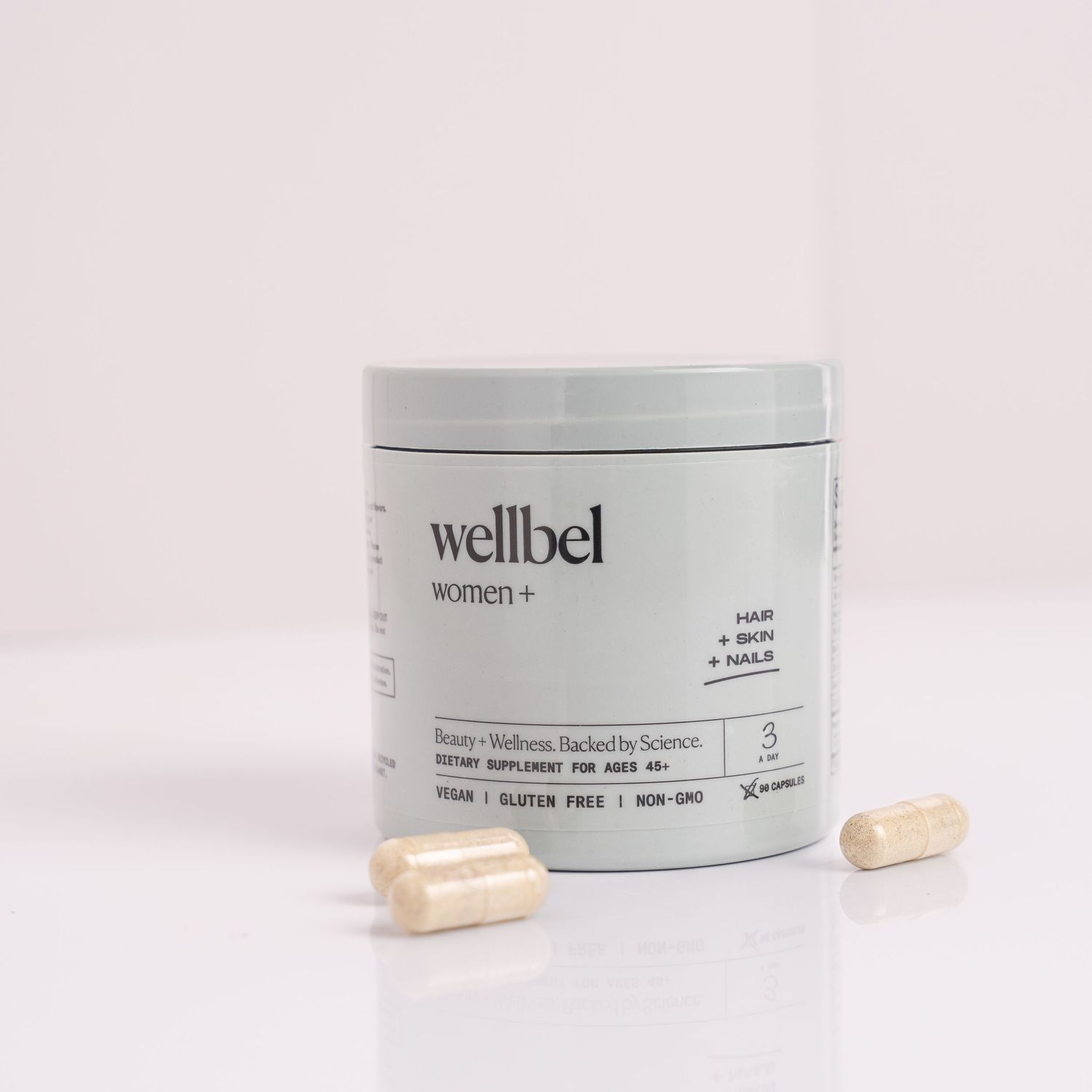 White supplement bottle and capsules arranged on light pink background showing wellness product photography.