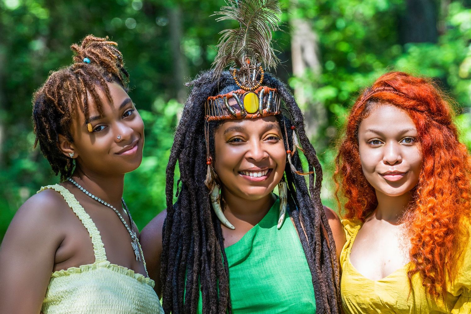 Three black women with vibrant loc hairstyles smiling together in outdoor setting for Honeysuckle Moon.