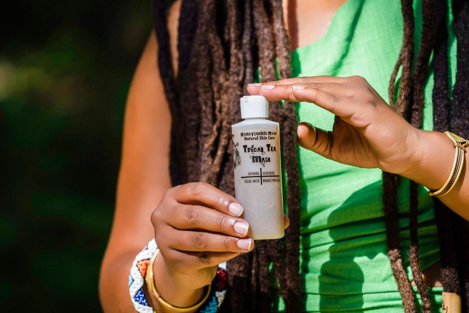 Hands holding a bottle of hair care product against green background.