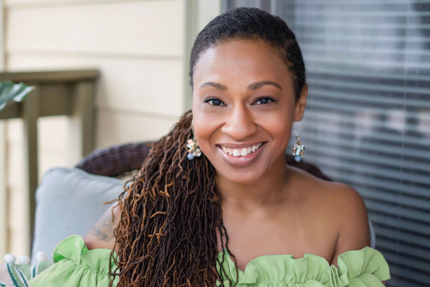 A person in a bright green blouse smiles warmly while sitting in an office setting.