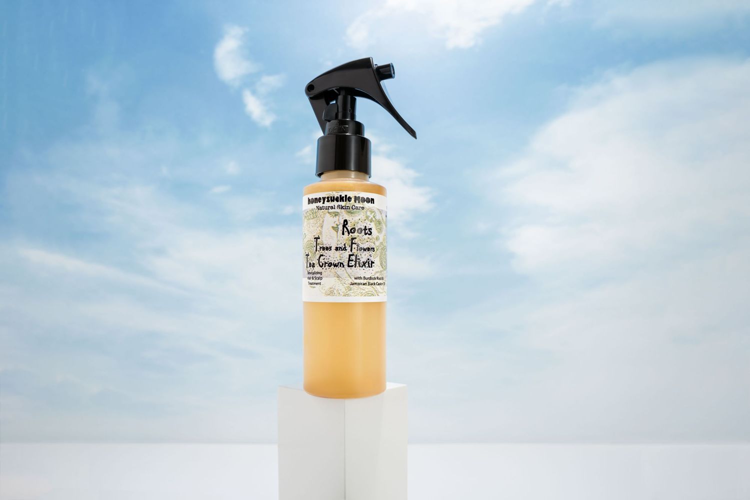 An amber-colored hair care product in a clear spray bottle photographed against a bright blue sky background.