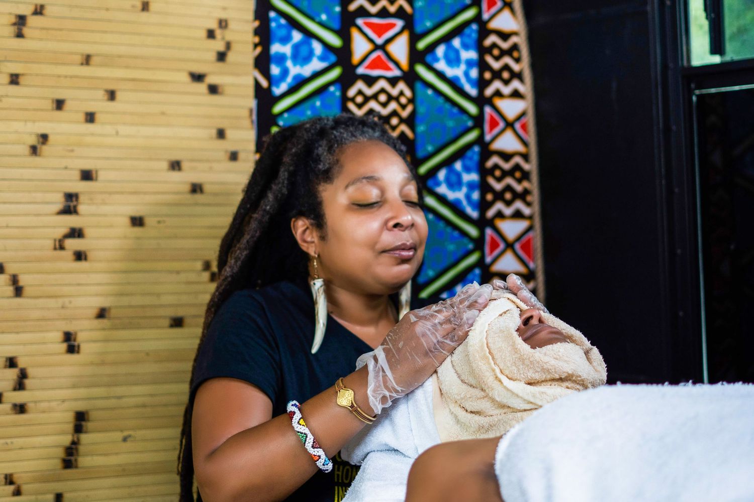 Honeysuckle Moon working on a client's facial in a spa setting with colorful African art in the background.