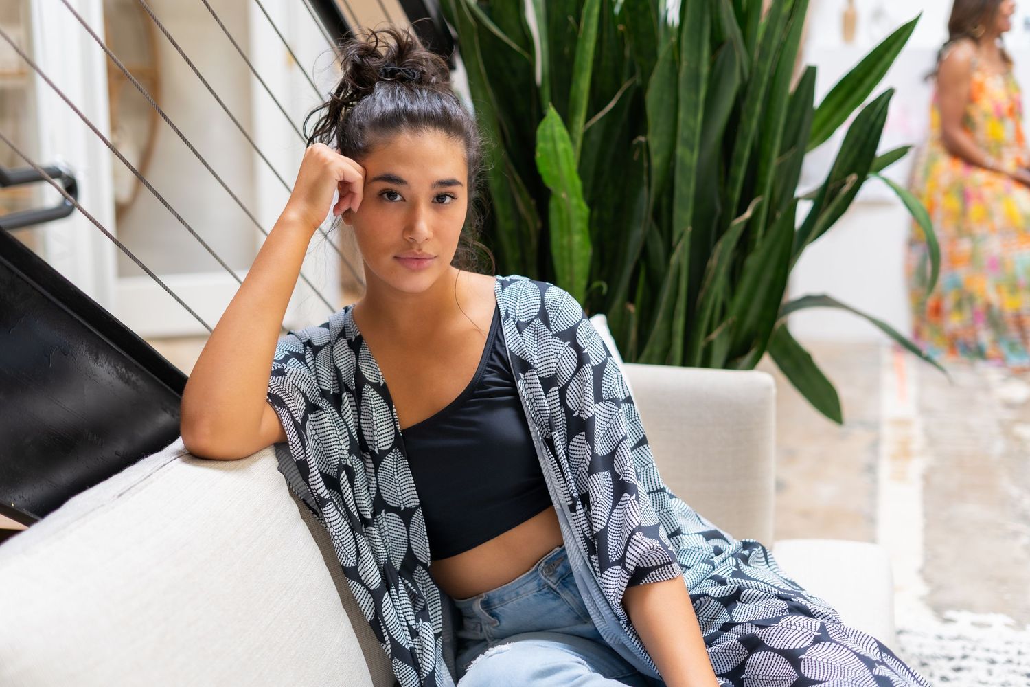 Woman in black sports bra and gray patterned jacket poses during workout session at home.