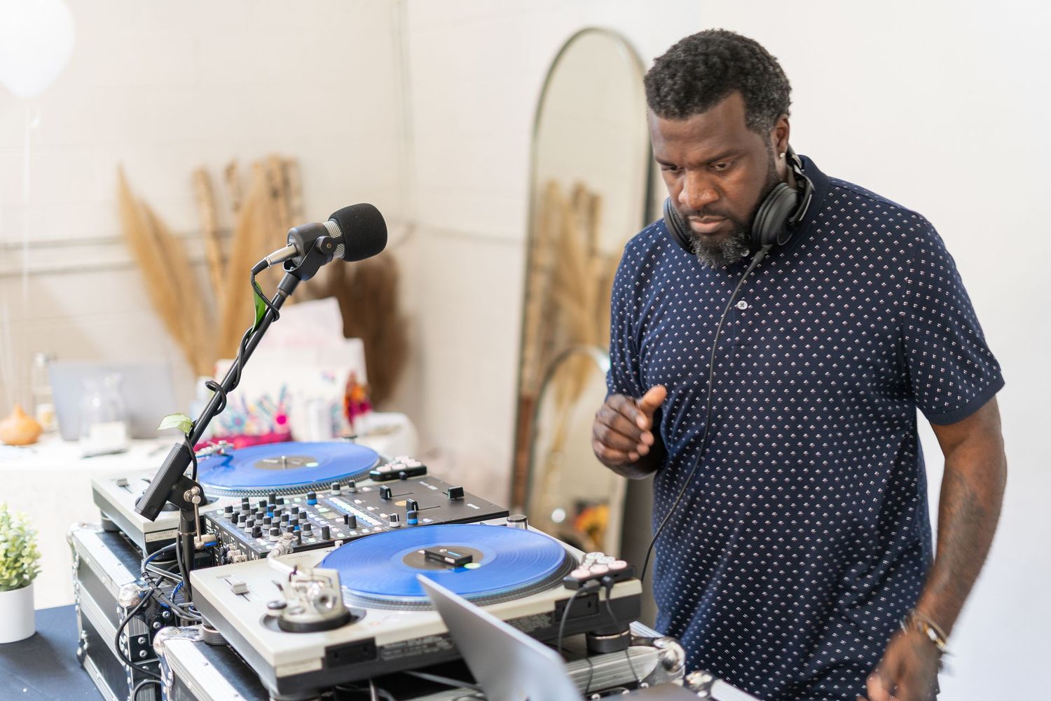 DJ in a navy polka dot shirt performs at an event using professional turntables and mixer equipment.