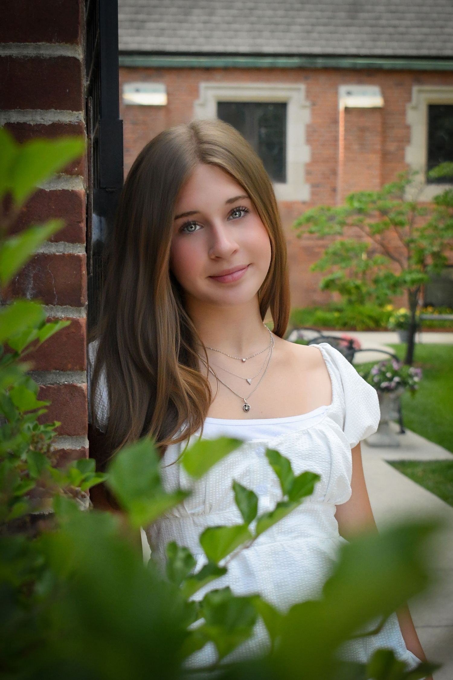 Senior photo with natural light beside brick wall and garden backdrop