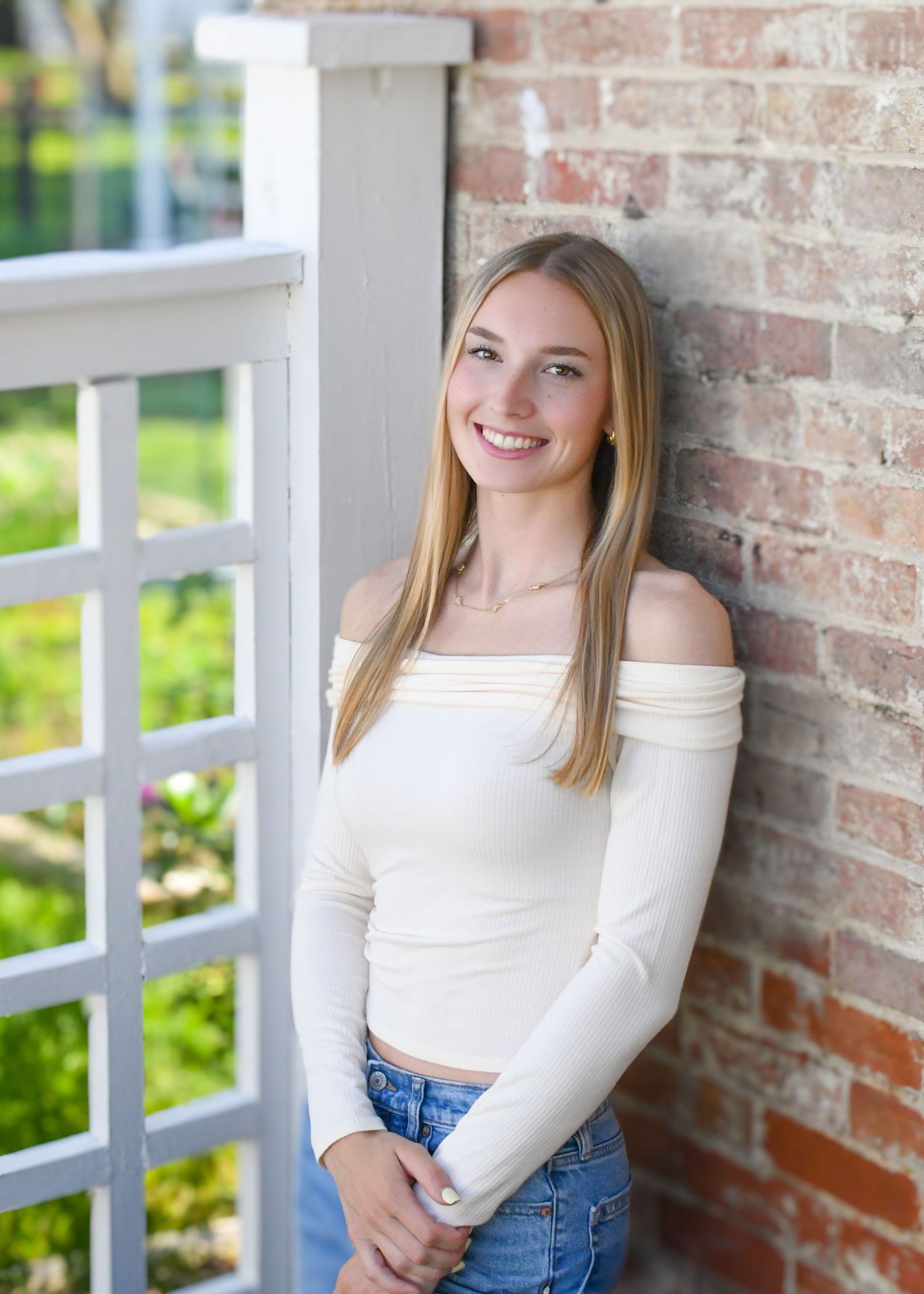 Senior photo with natural light beside brick wall and garden backdrop