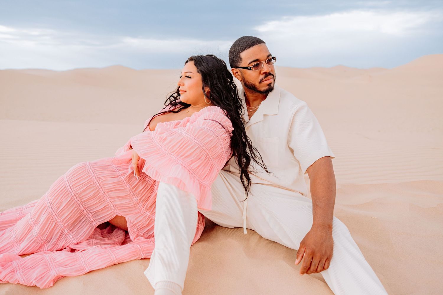 Couple in coordinated outfits poses intimately against desert sand dunes during sunset photography session.