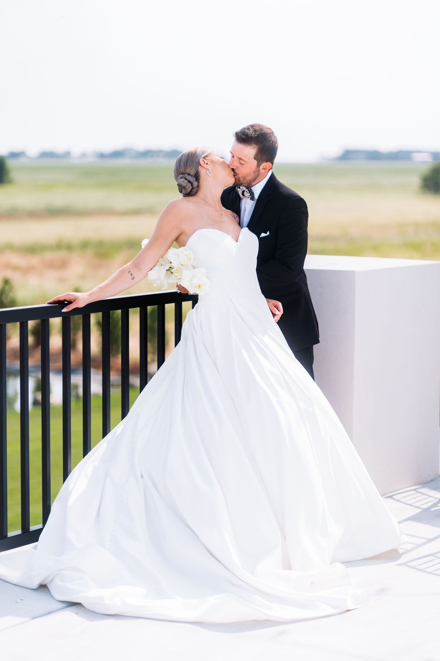A romantic wedding pose against a bright outdoor backdrop with flowing white gown.