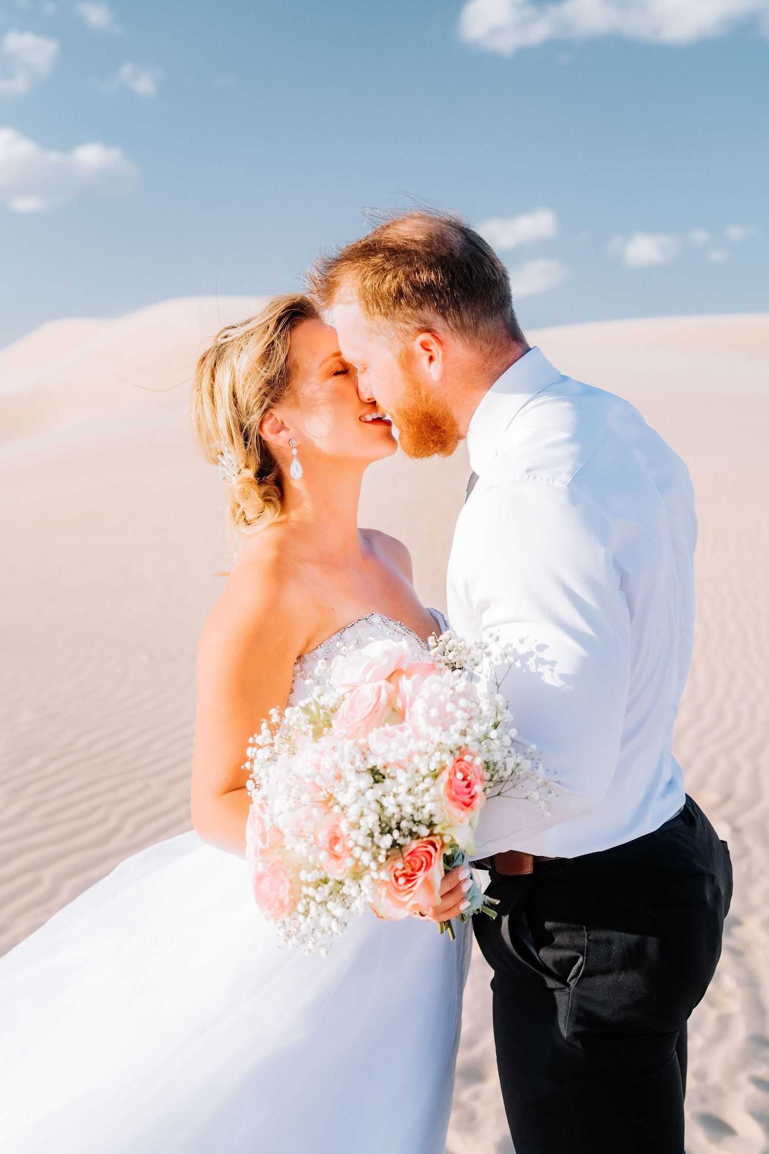 Romantic couple sharing intimate moment in desert setting with bridal bouquet.