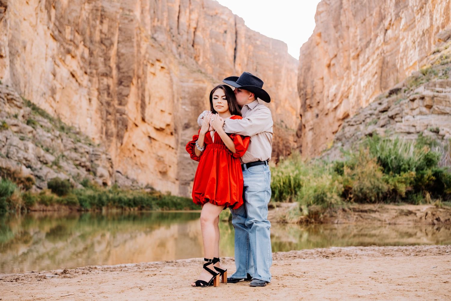 Couple dancing together by a scenic canyon lake, woman wearing vibrant red dress.